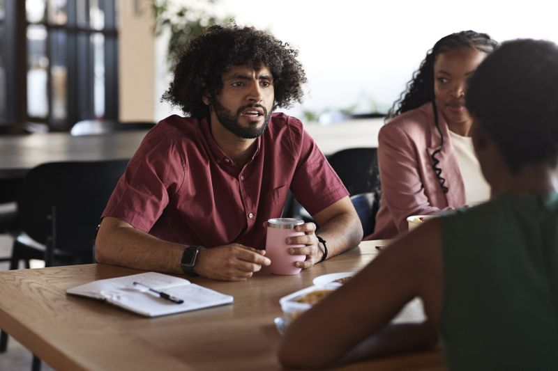 Three people sitting at a table and chatting with food and drinks present
