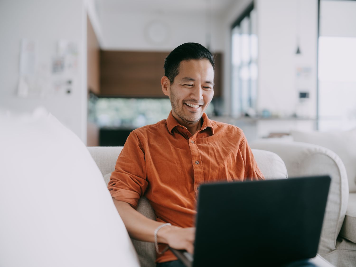 A happy man looks at his laptop while sitting on a couch.