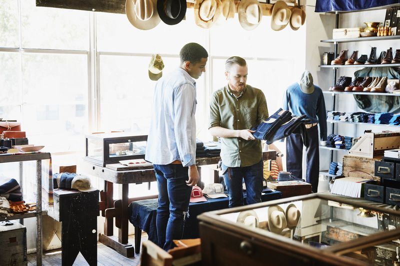 A boutique shop owner shows a customer some jeans.