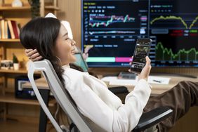 Happy woman sitting at a desk looking at charts on her mobile device. 