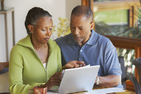 Couple in their 40s or 50s sitting at a table at home looking at mortgage rates on a laptop