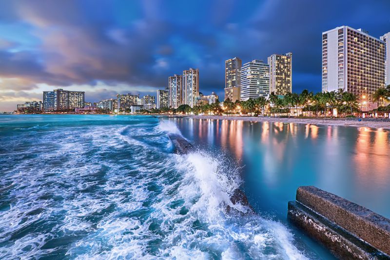 Waves surge toward Waikiki’s beaches in the blue hour in Honolulu, Hawaii.