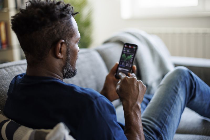 Man sitting on his couch looking at a chart on his phone