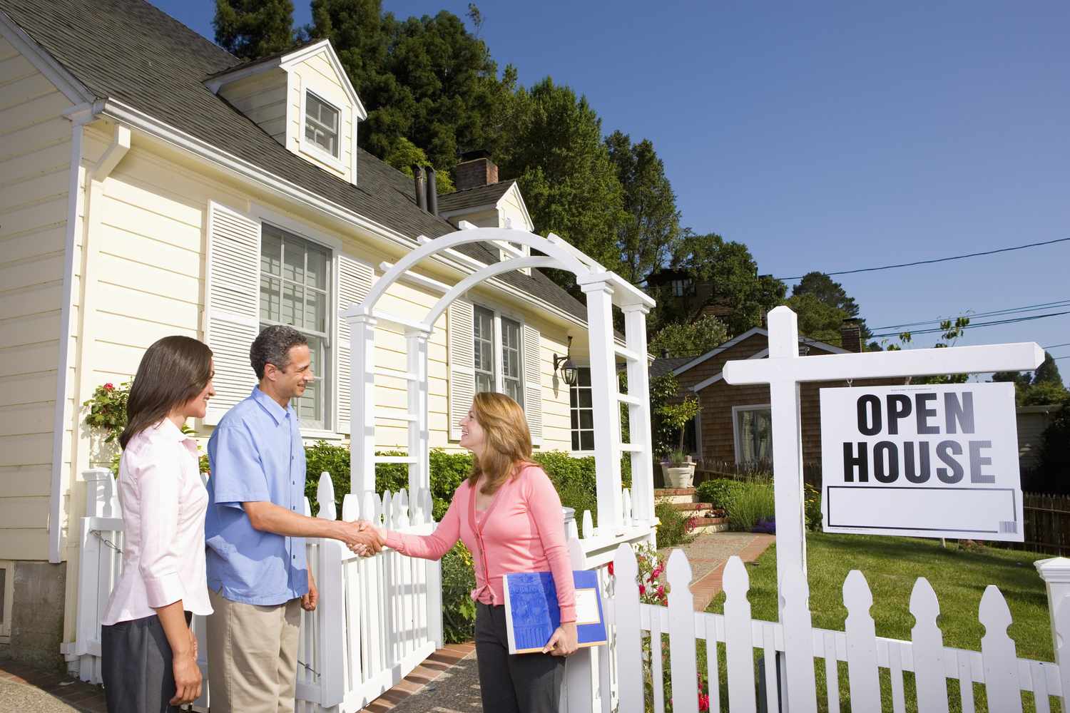 Homebuyers shaking hands with realtor outside home for sale