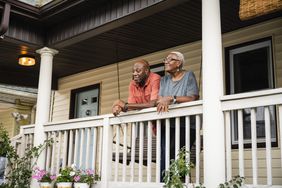 A man and a woman stand on the front porch of a house