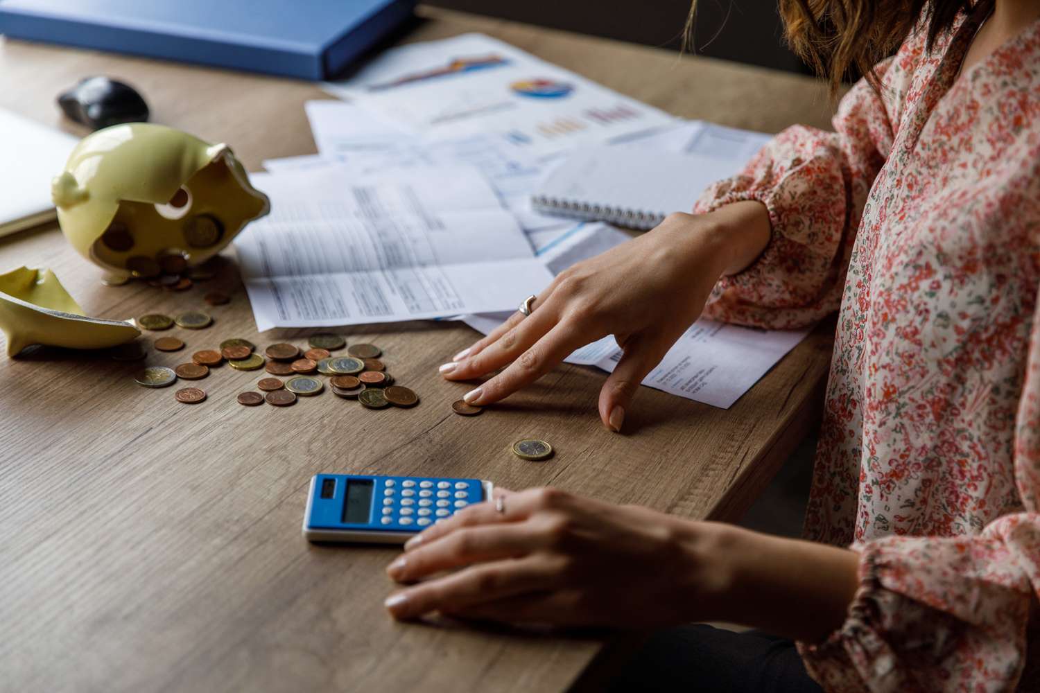Person using a calculator and counting coins with paperwork in background.