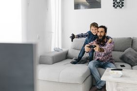 a father and son playing a video game on the couch