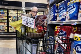 Person shopping in a grocery store, reading a flyer while leaning on a cart near the dairy aisle