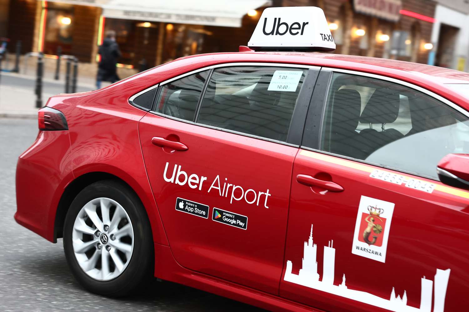 The Uber Airport logo is seen on the side of a red car with an Uber Taxi sign on top of the car.