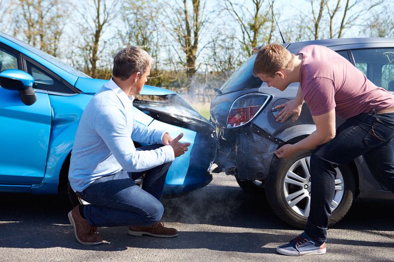 Two men look at their damaged cars after an accident