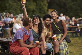A group of four young adults sitting together, smiling and holding cups outdoors