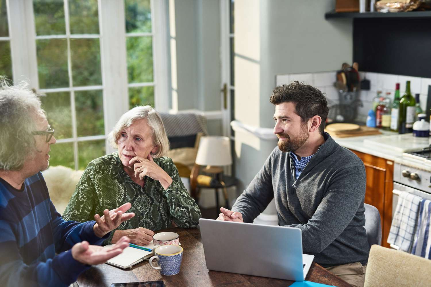 A financial advisor discusses bond yield with a mature client couple while sitting around a kitchen table.