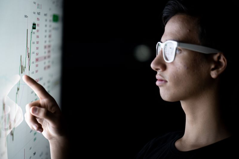 An investor pointing at a monitor showing securities price details 