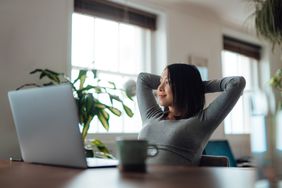 An investor with raised arms, taking a break while using laptop in the living room. 