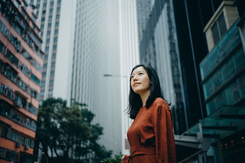 Low-angle portrait of a confident young woman standing against high-rise buildings in a city.