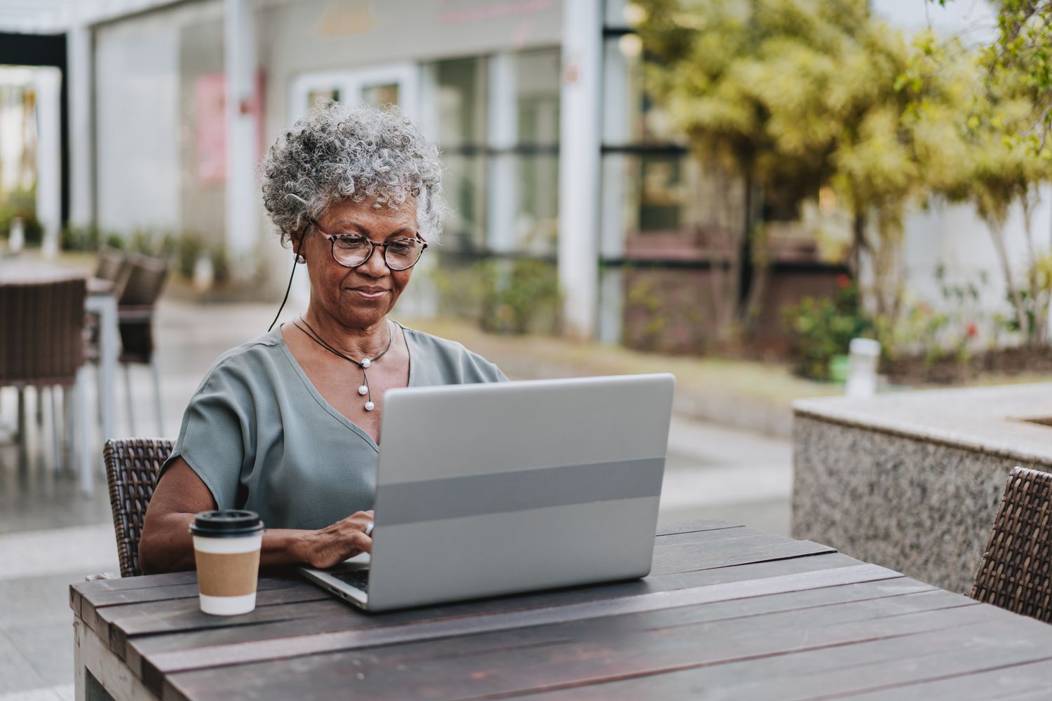 Older woman with a laptop and a coffee cup outside