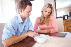 Couple in their 30s sitting in their dining room and looking at mortgage documents and a tablet