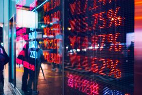 People standing outside at night in front of stock ticker sign