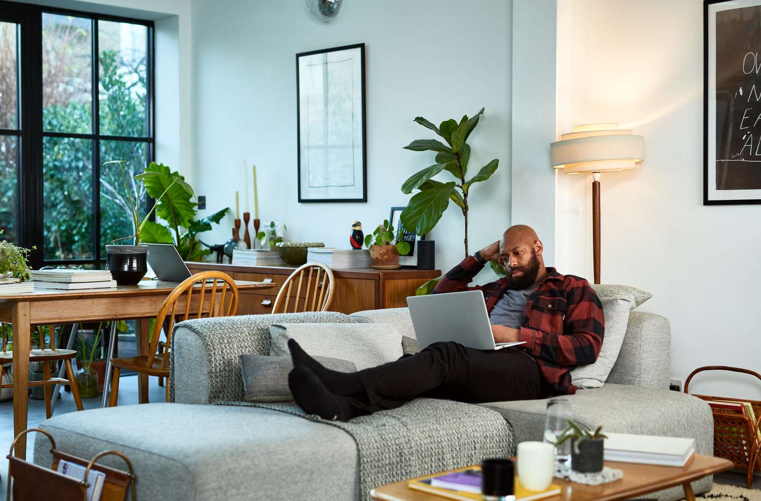 A man sits with his legs up on a couch with a laptop on his lap