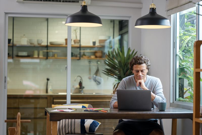 Man using a laptop at a home office with a kitchen in the background