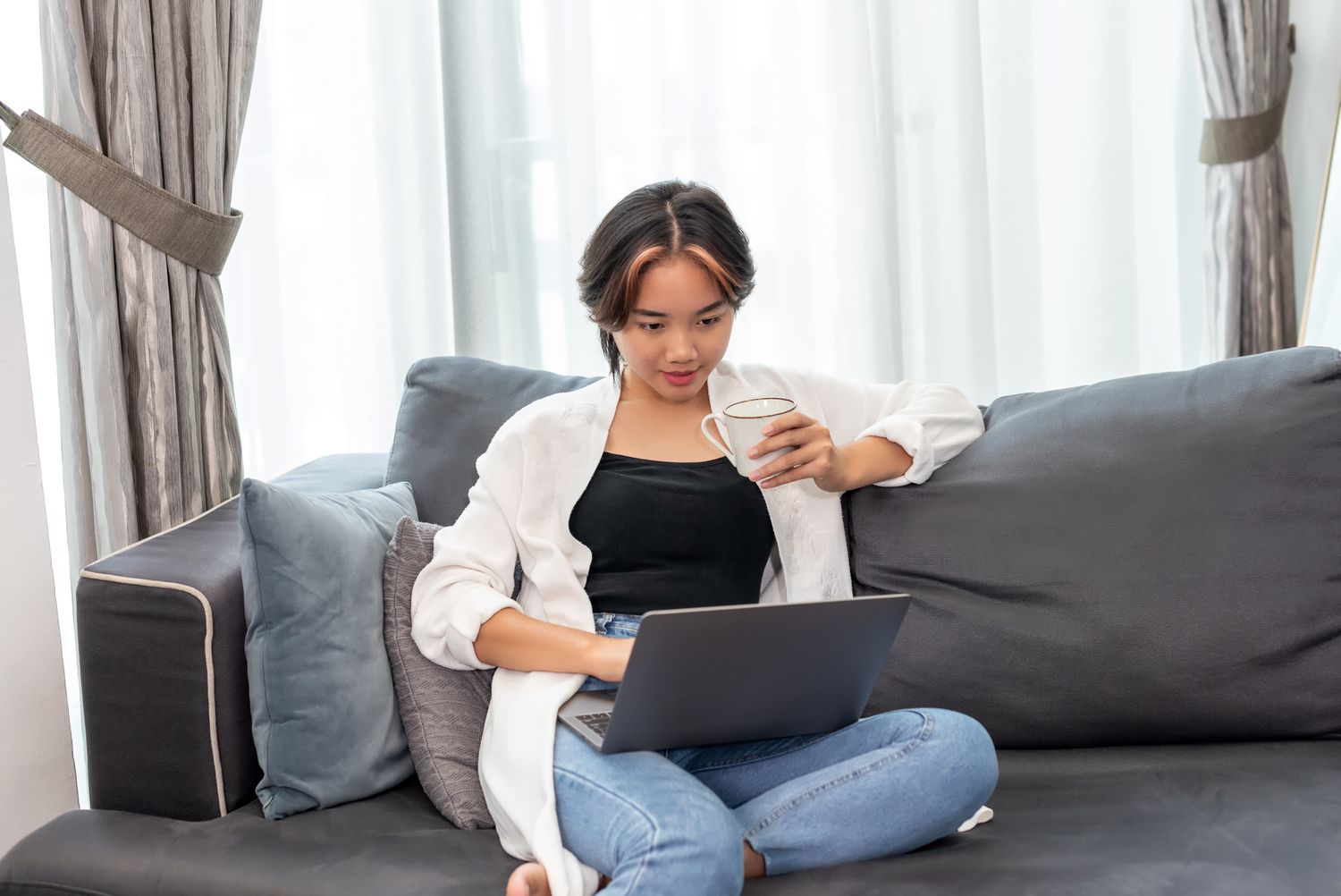 person sitting on couch in jeans and white shirt looking at computer