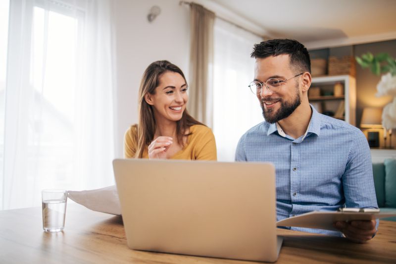 Young couple sitting at their dining table and looking happily at mortgage rates on a laptop