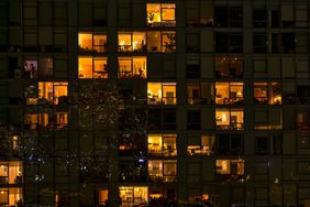 View of apartment windows at night as seen from the Brooklyn Bridge with lights from the bridge reflected on the outside of the apartment building in Brooklyn. From the Brooklyn Bridge walkway one can see directly into the illuminated apartments of this building on the Brooklyn side of the bridge at night.