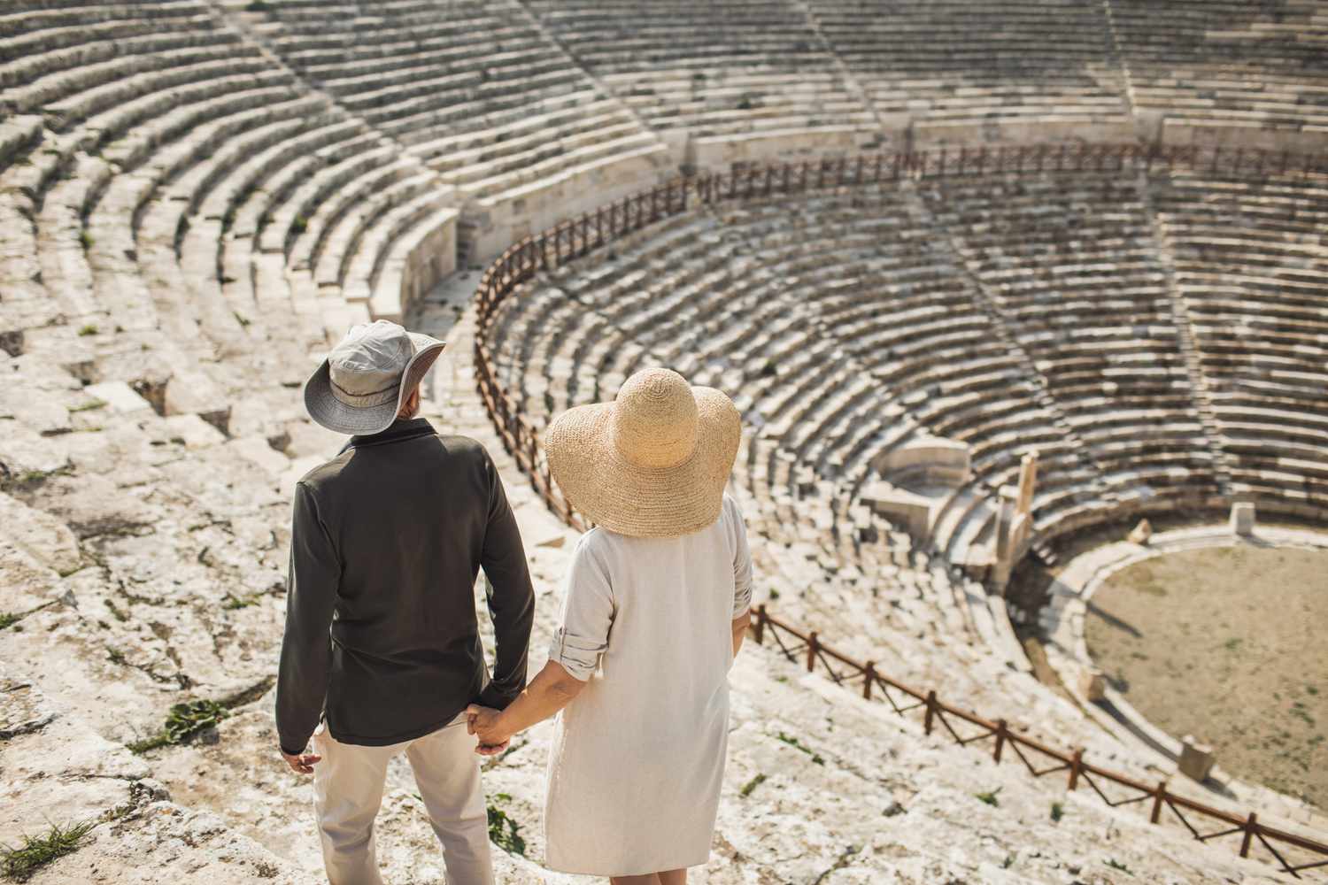 Older couple holding hands, overlooking old stone theater.