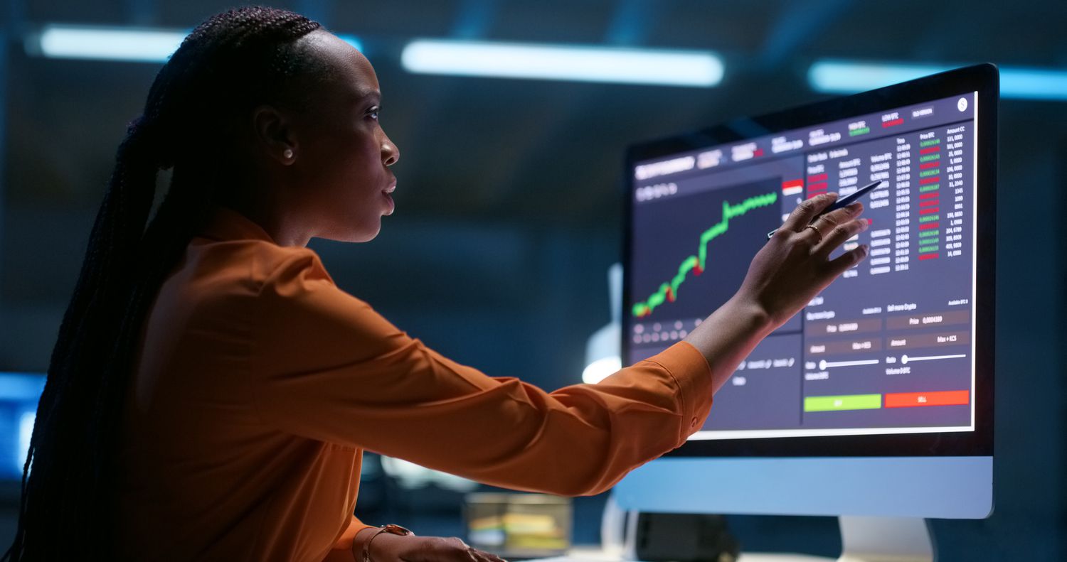Woman sitting at a desk working on a large computer with charts and data.
