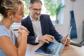 Older man explaining something on a laptop to a younger woman