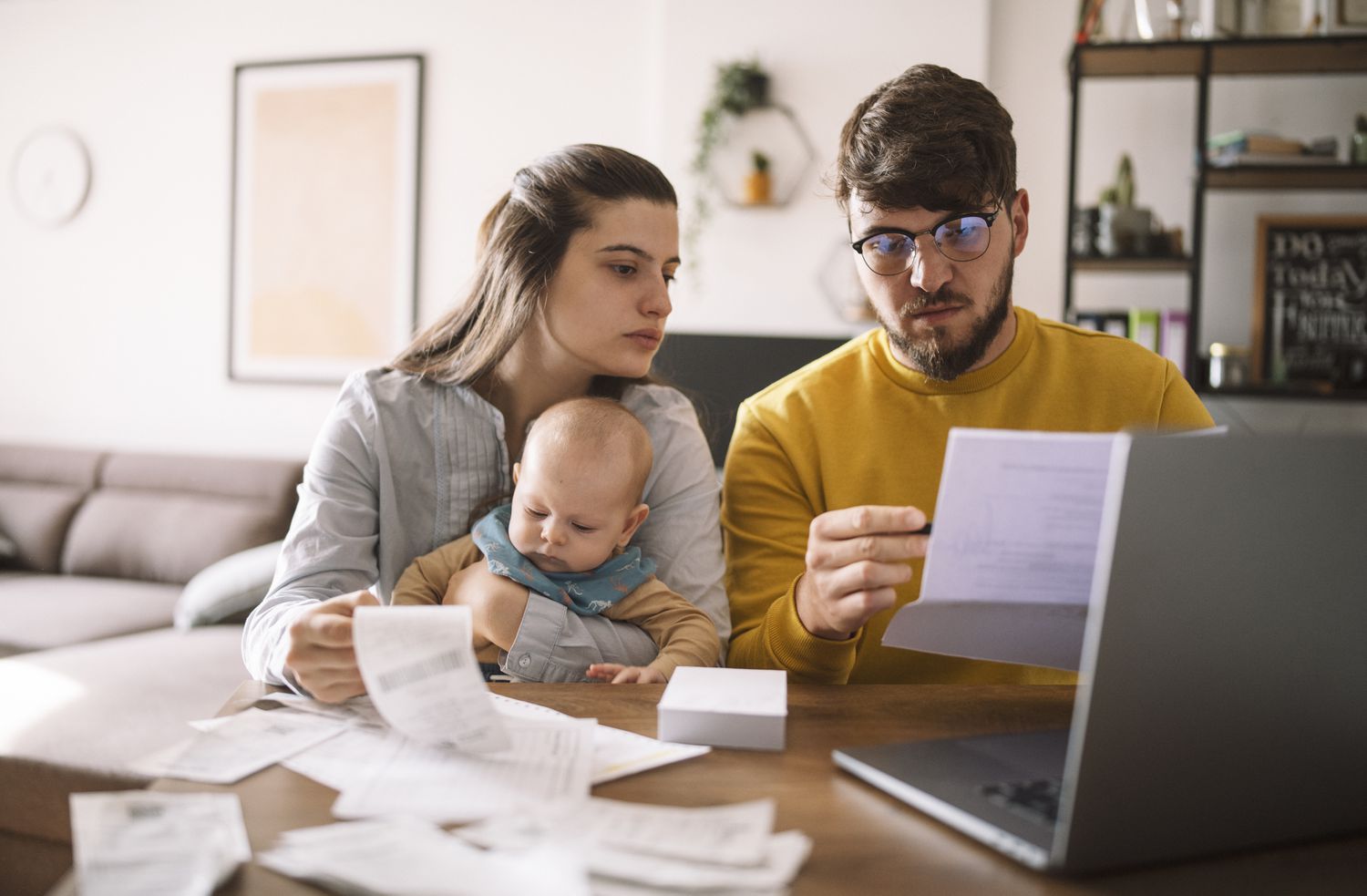 A young couple with a baby sit at the dining room table going over a family budget.
