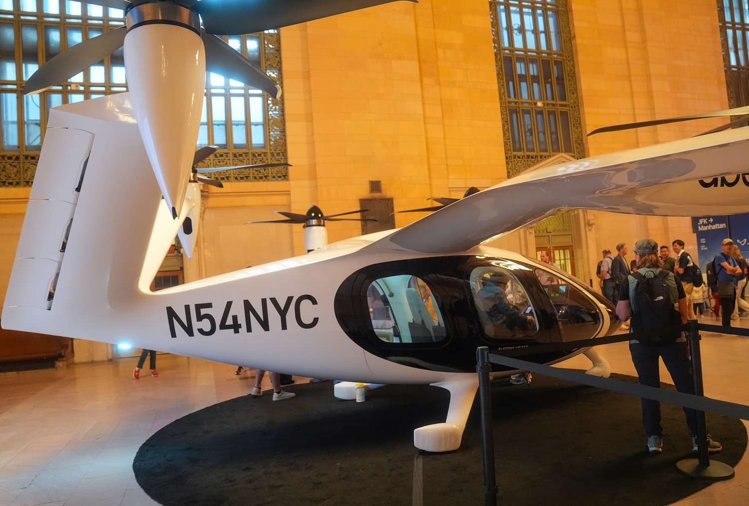 People stand around looking at a white and black Joby electric air taxi helicopter inside a building.