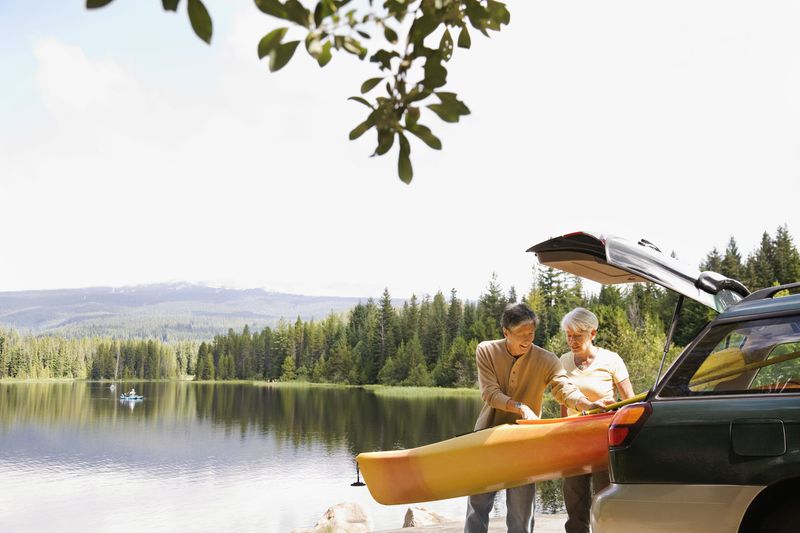 Elder couple taking a kayak out of the back of their car by a lake