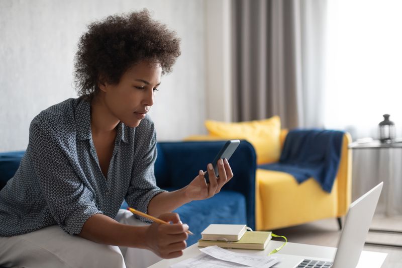 Woman looking at a smartphone while working at a laptop