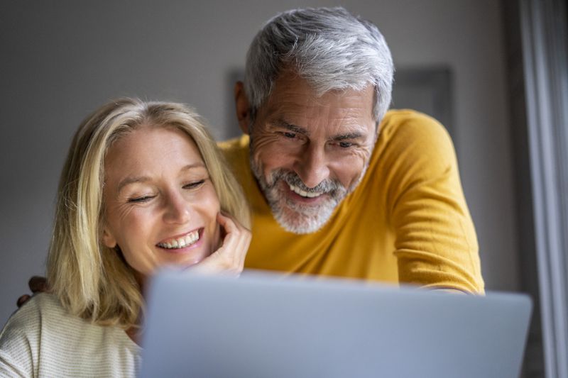 Older couple at home and smiling as they look together at mortgage rates on a laptop