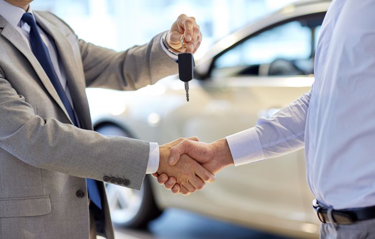 Close up of dealer giving key to new owner and shaking hands in auto show.