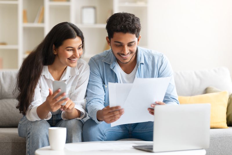 Young couple sitting on their sofa and looking at mortgage documents and rates on their laptop