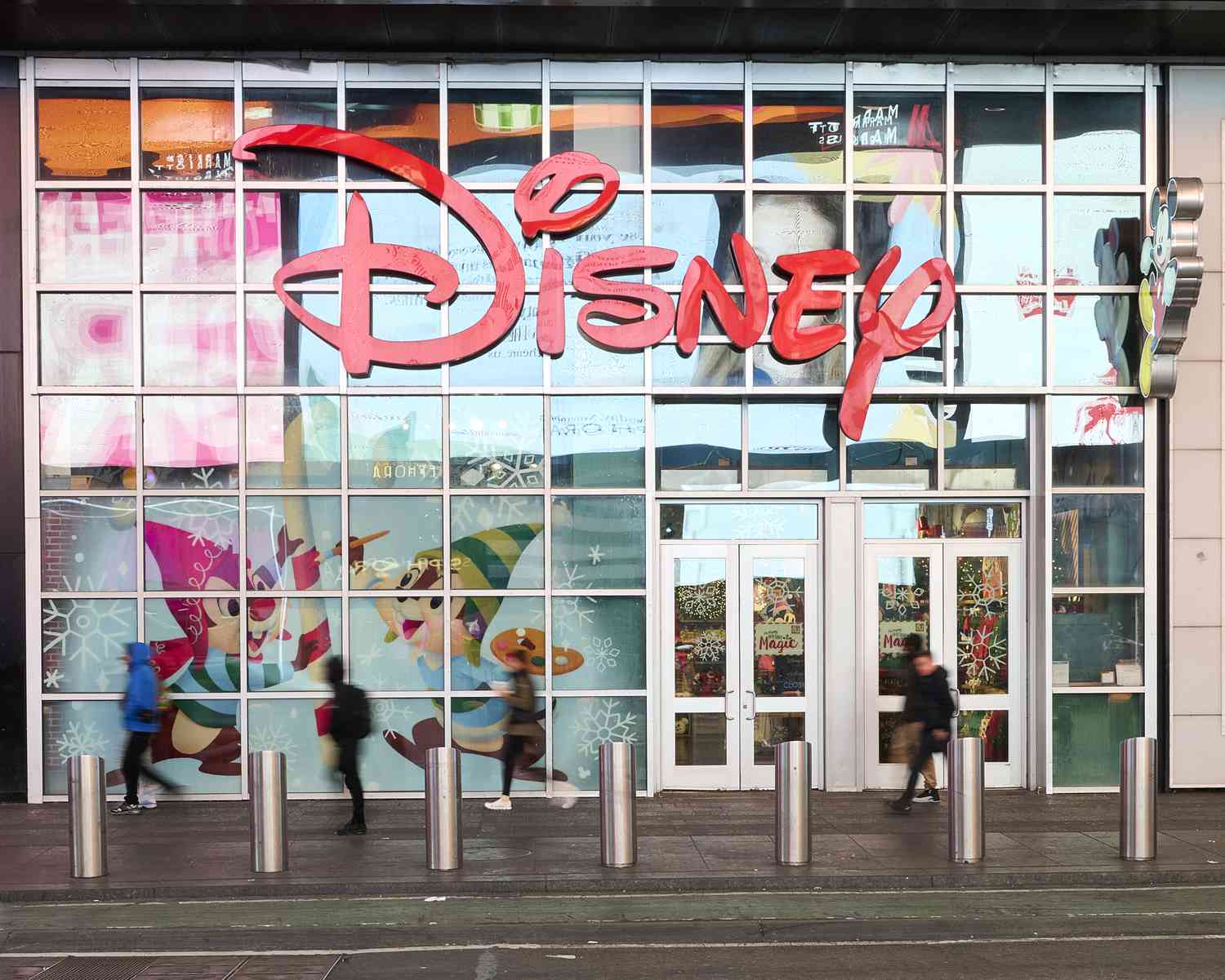 People walk in front of the Disney store in Times Square, with a red Disney logo above the door.