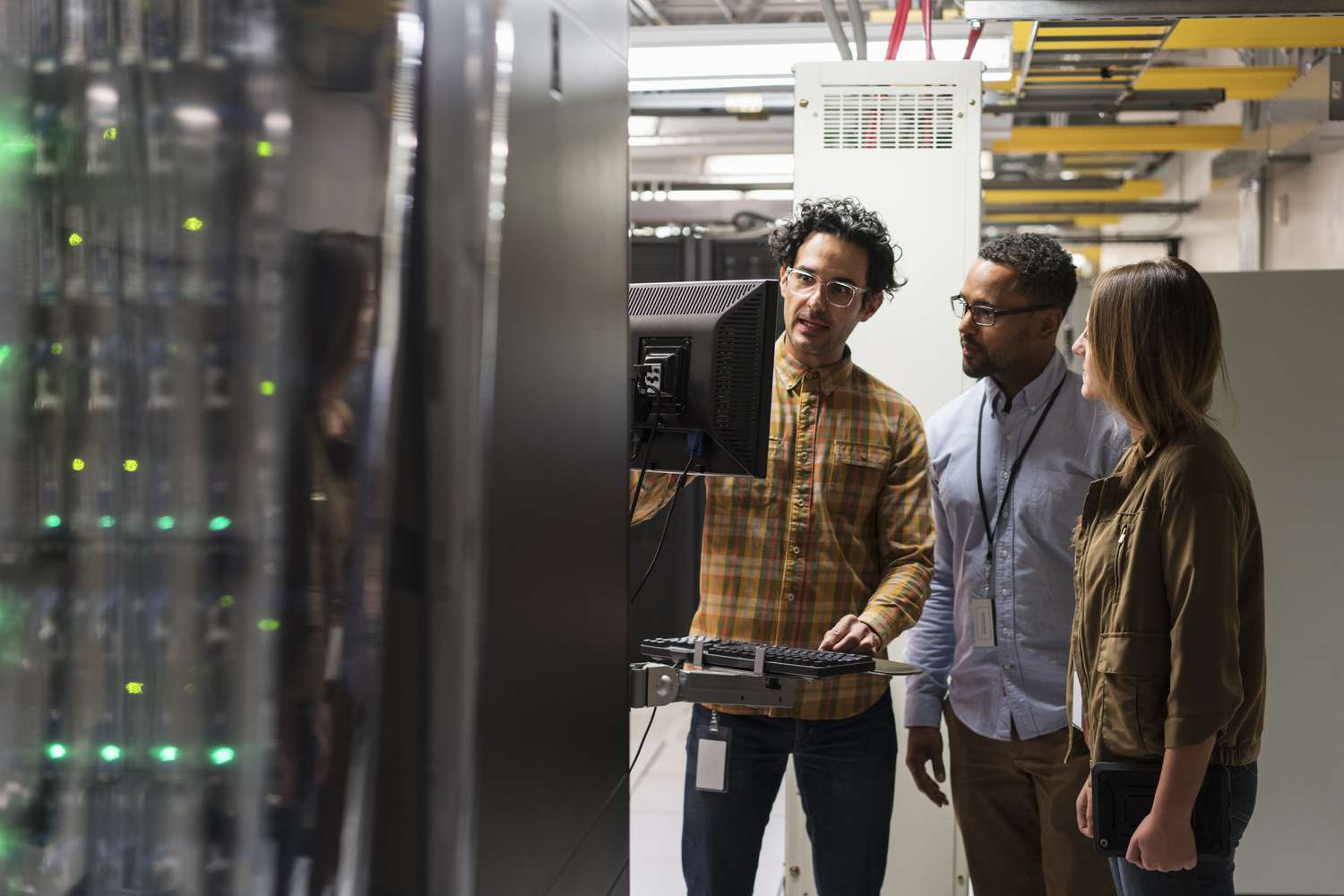 Three technicians use a computer terminal in a server room.