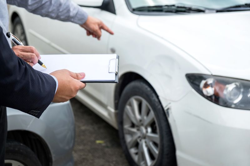 Midsection Of Owner Pointing Towards Car While Signing Paper With Agent