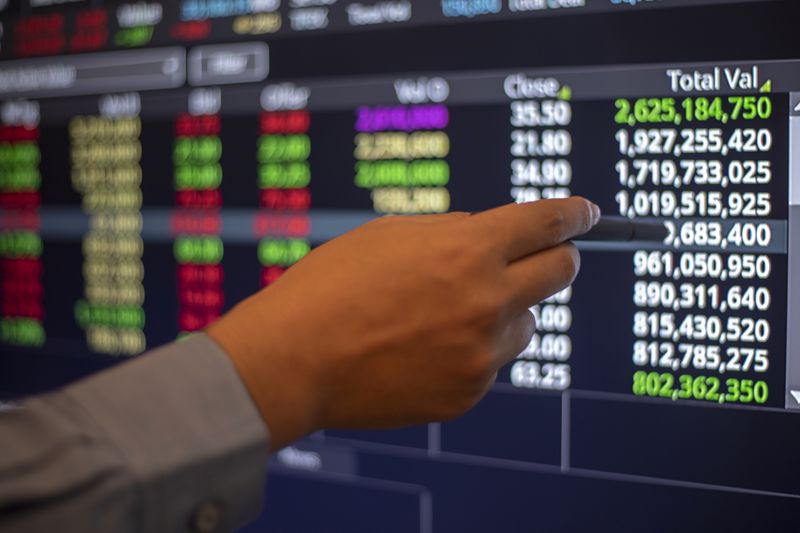 A person's hand holding a pen pointing to stock data