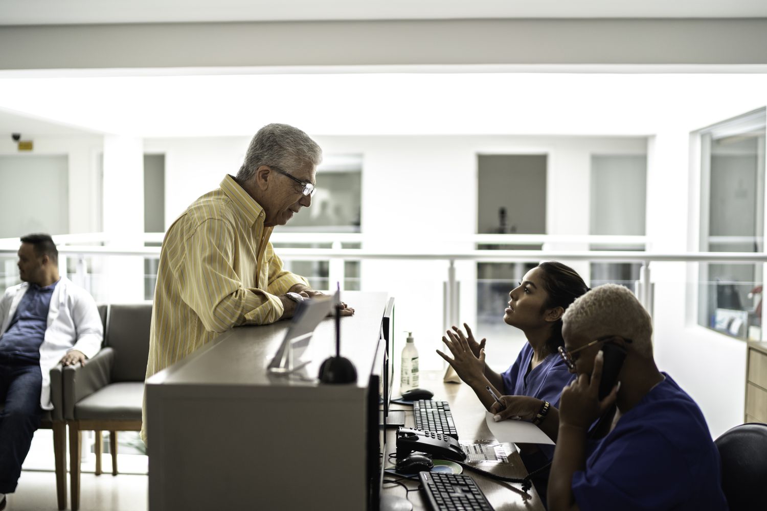 Older patient talking to a woman in scrubs at a desk