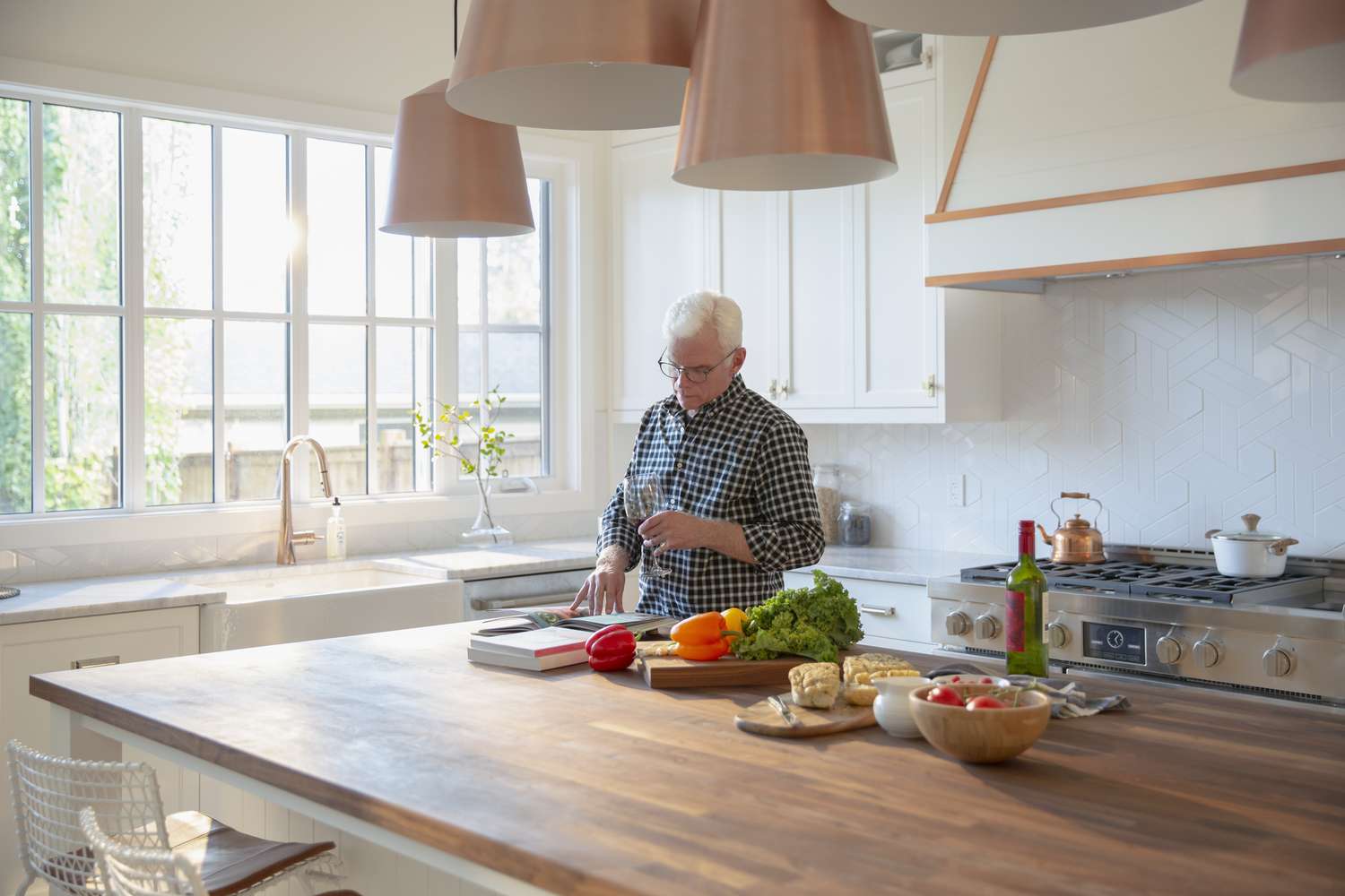 Older man cooking, drinking wine and looking at cookbook in kitchen