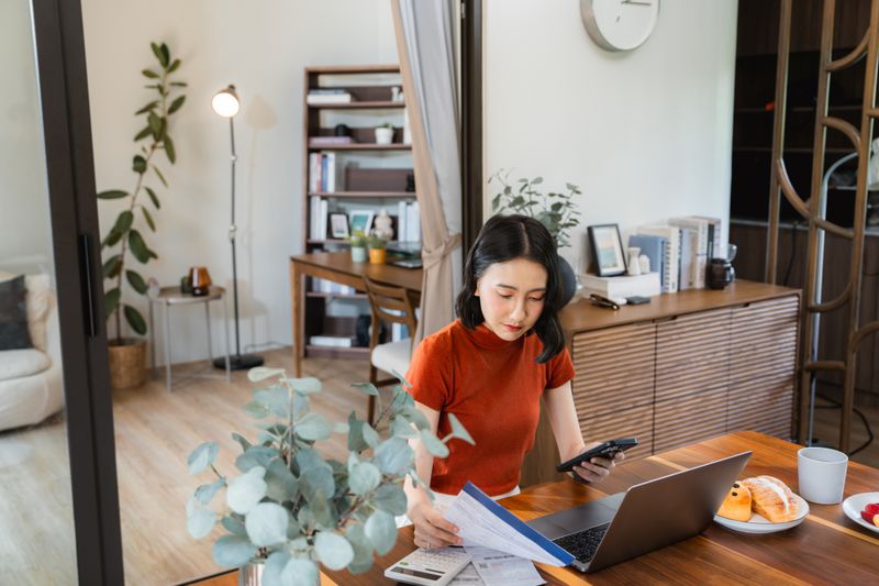 A person doing personal finances and checking current liens on laptop at home, surrounded by papers and food in a cozy room.