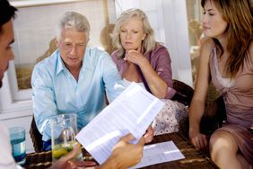 An older couple and a younger woman sit down with a man at a table at home while they review the information on a piece of paper. 