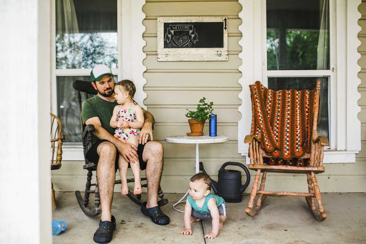 Sister sitting on father's laps while brother crouching at porch - stock photo