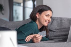 A smiling woman relaxes on the couch, holding a bank card.
