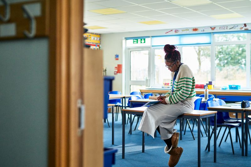 Primary school teacher waiting for class to start, in empty classroom, marking homework, looking at book