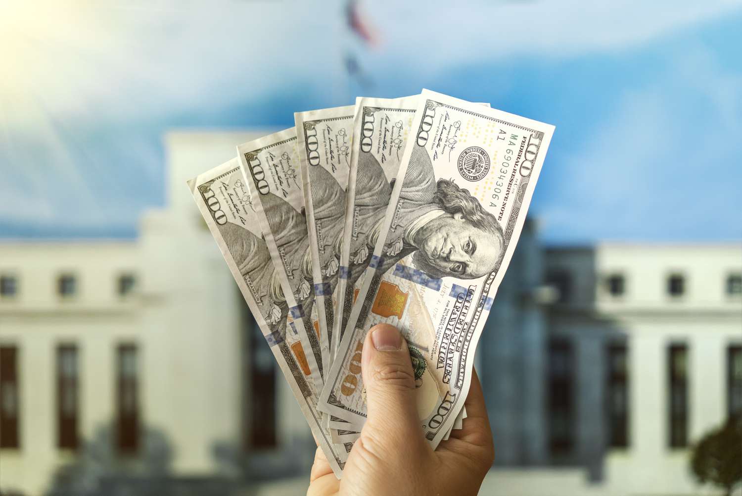 A person holding up U.S. currency in front of the Federal Reserve Building