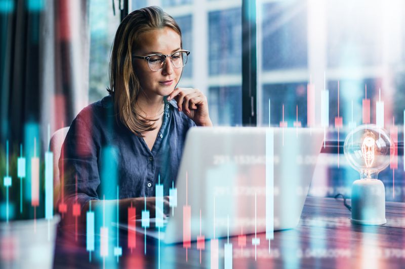 Businesswoman working in an office with a laptop on her desk, overlaid with financial bar graph